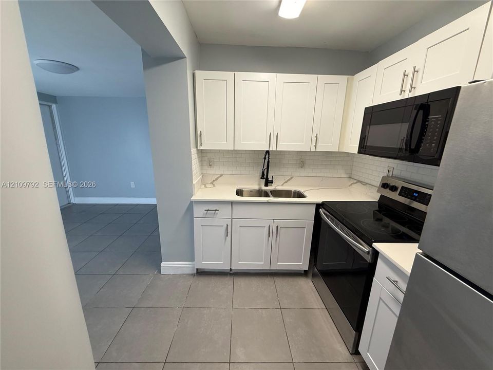 Kitchen featuring white shaker-style cabinetry, white countertops with grey veining, a white subway tile backsplash, a dual-basin stainless steel sink with a matte black faucet, and stainless steel appliances