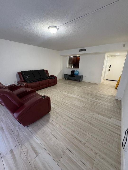 Open-concept space featuring light-toned wood-finish tile flooring, a centered ceiling-mounted light fixture, and a kitchen pass-through window
