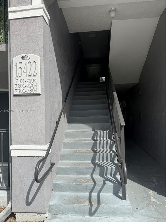 Stucco exterior featuring concrete stairs with dual metal handrails and a mounted building identification plaque