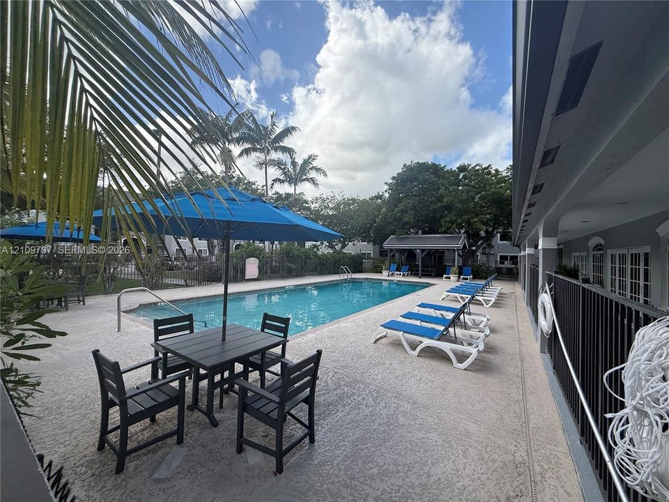 Swimming pool with a paved deck, perimeter metal fencing, and a covered pavilion