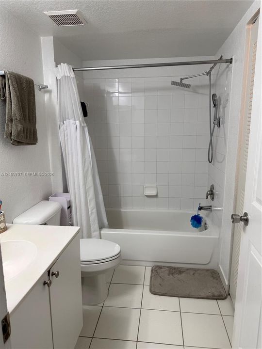 Bathroom featuring a white vanity cabinet, square tile flooring, and a tub-shower combination with white wall tile, a rainfall showerhead, and a handheld attachment