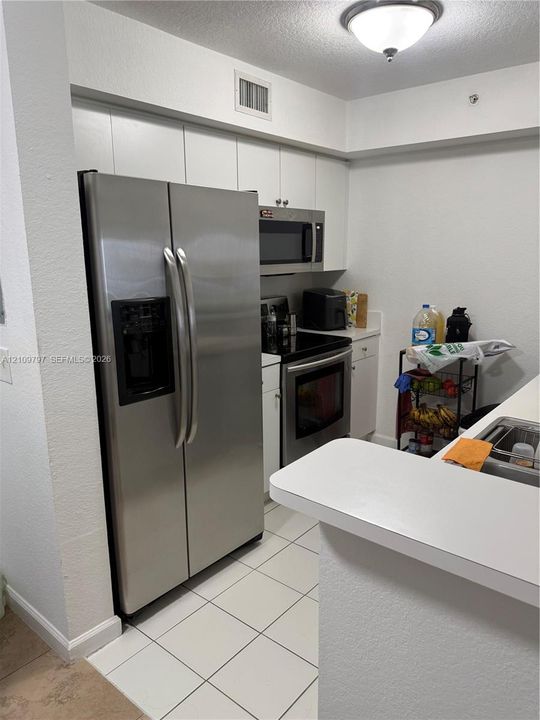 Kitchen featuring stainless steel side-by-side refrigerator, over-the-range microwave, range with ceramic glass cooktop, white cabinetry, and tile flooring