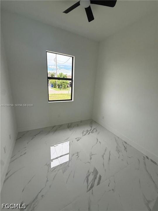 Interior room featuring large-format stone-patterned floor tile, neutral wall paint, and a matte black ceiling fan