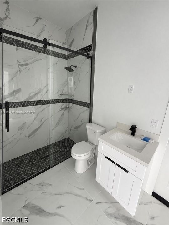 Walk-in shower with floor-to-ceiling stone-pattern tile, hexagonal mosaic tile flooring, glass enclosure with matte black hardware, white vanity cabinet with light-toned countertop, and matte black plumbing fixtures