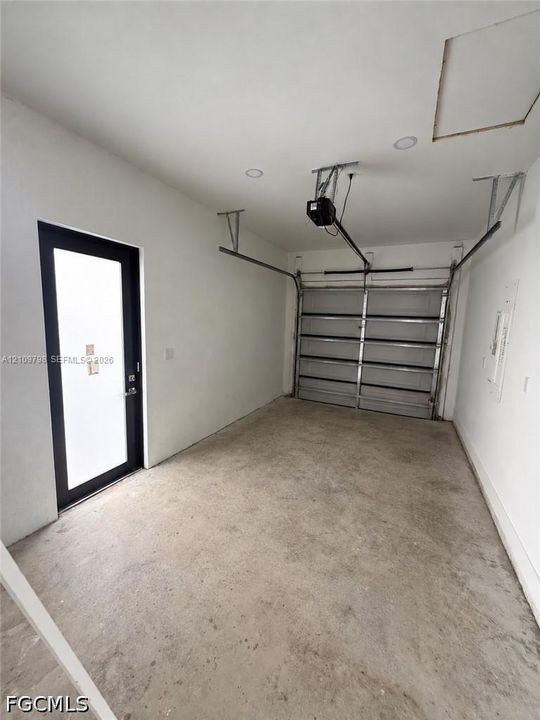 Enclosed garage featuring concrete flooring, white walls, recessed ceiling lighting, and a side-entry door with a black frame