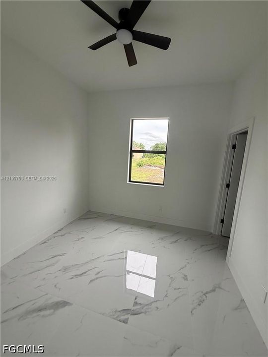 Interior room featuring large-format tile flooring with a neutral veined pattern, matte black ceiling fan, and a single-pane window