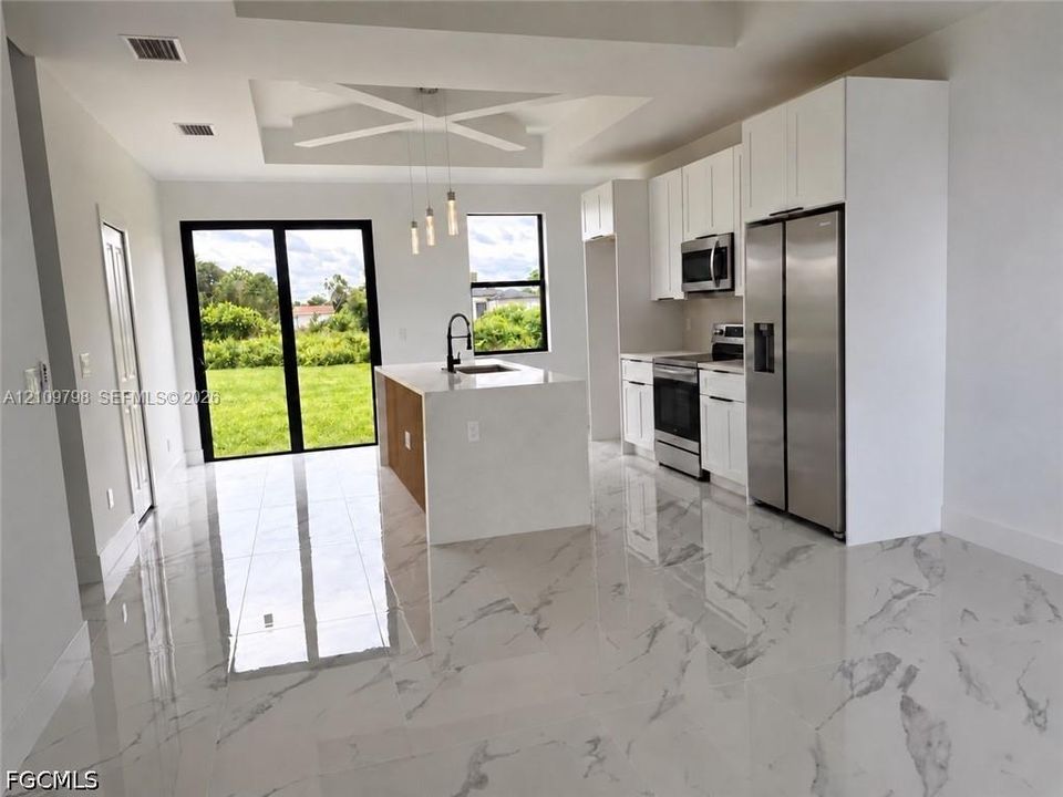 Kitchen featuring white cabinetry, an island with stone-finish countertops, stainless steel appliances, a coffered ceiling, and large-format tile flooring