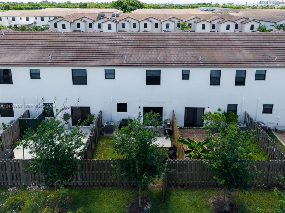 Two-story townhome exterior featuring white stucco siding, a tiled roof, private fenced rear patios, and rear-entry sliding glass doors