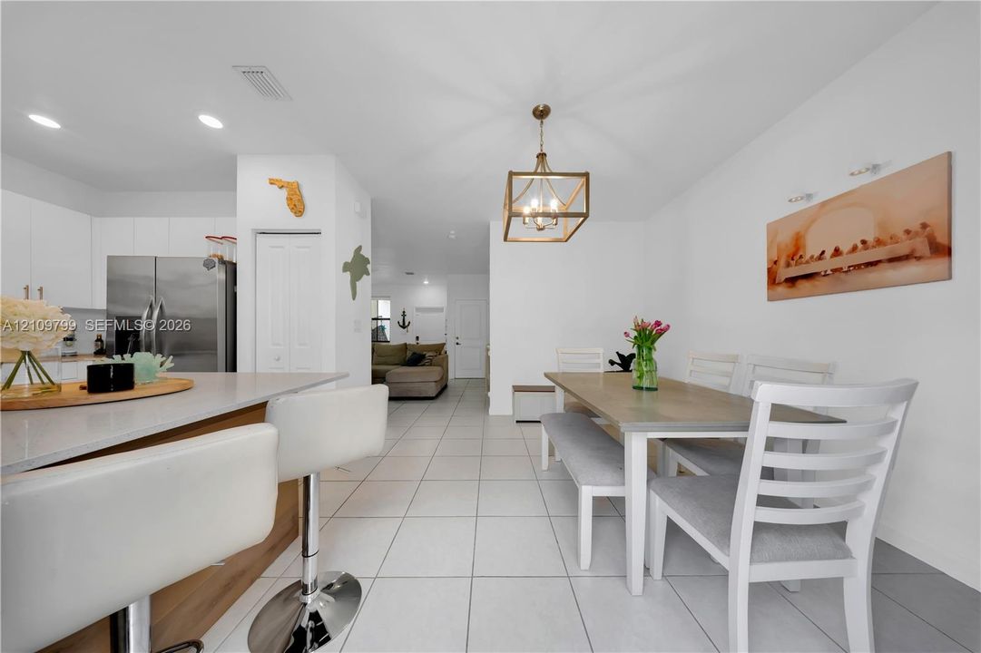 Kitchen featuring a peninsula with stone-look countertops, stainless steel refrigerator, recessed lighting, and a geometric pendant light fixture, complemented by light-toned tile flooring
