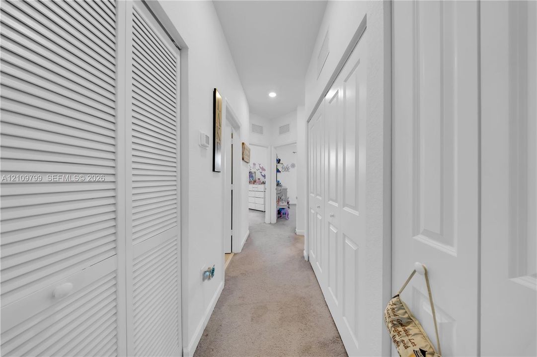 Hallway featuring dual sets of white louvered-style closet doors, recessed lighting, and neutral carpeting