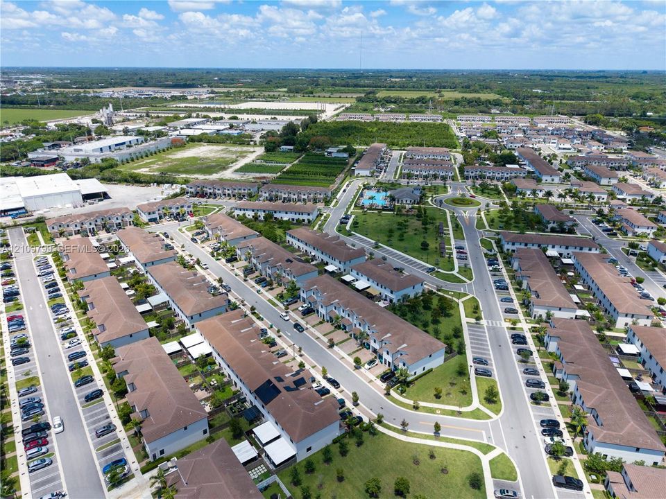 Aerial perspective of multi-unit residential structures featuring neutral stucco exteriors, hip-style roofs with brown shingles, designated parking areas, and landscaped community green space