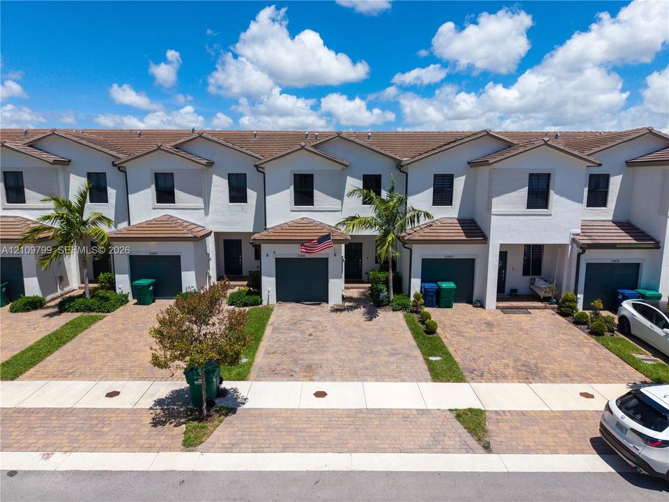 Stucco townhouse exterior featuring a multi-gabled tile roof and individual paver driveways