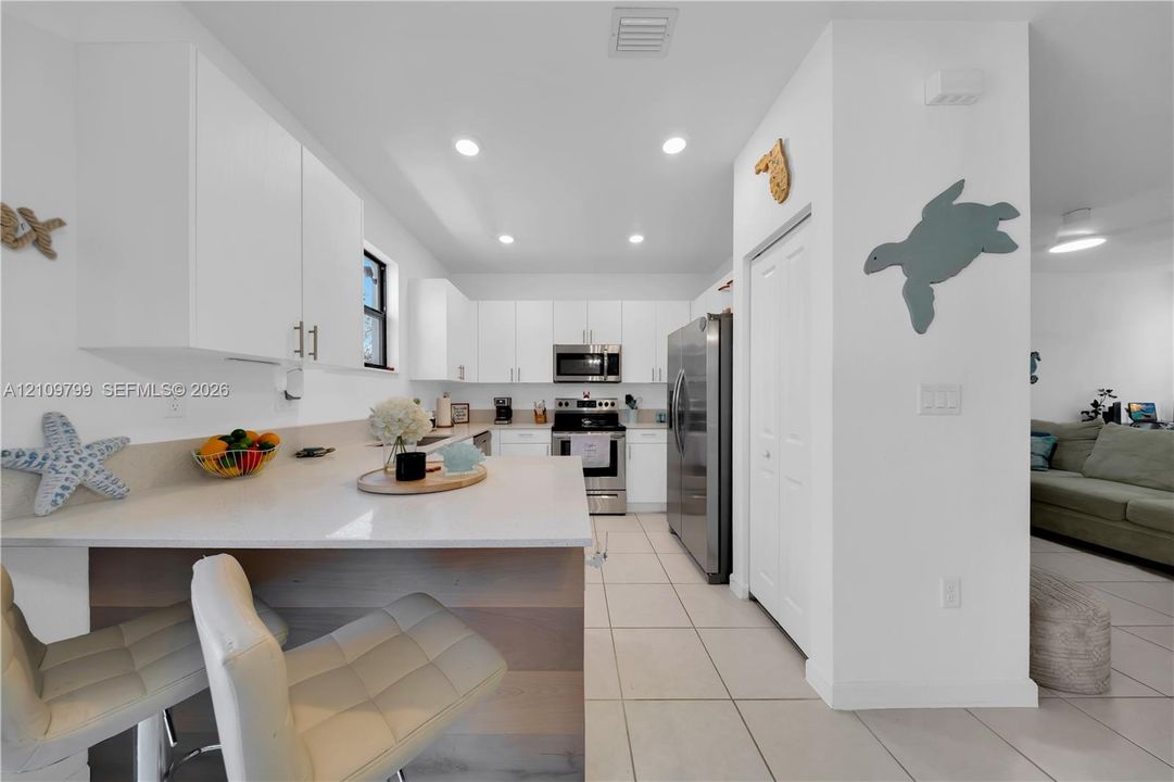 Kitchen featuring white cabinetry, quartz countertops, a stone-finish waterfall edge island, recessed lighting, and stainless steel appliances