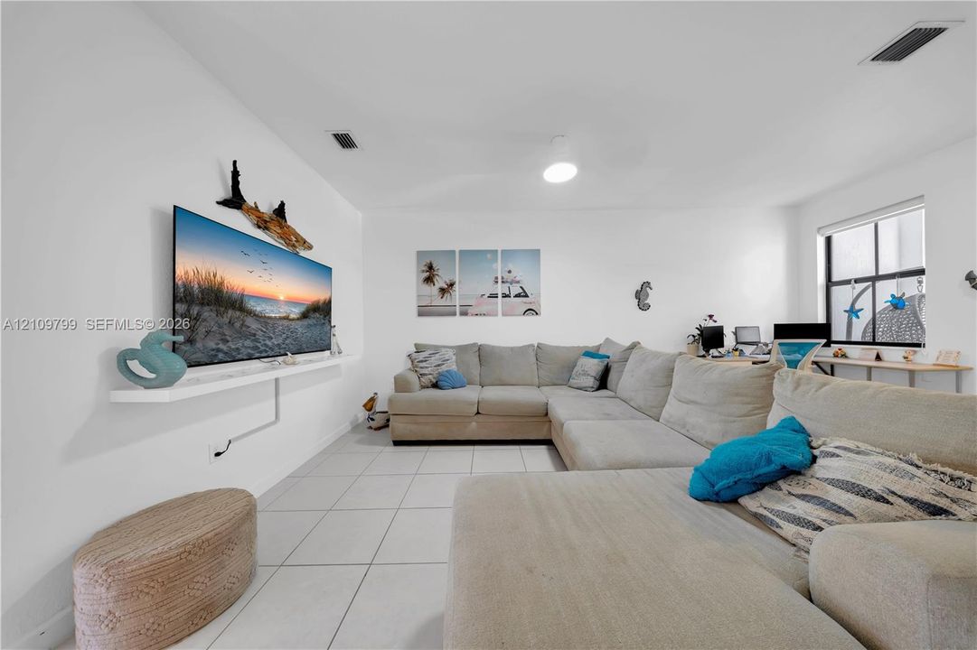 Living area featuring large-format ceramic tile flooring, a wall-mounted floating shelf, neutral wall tones, and windows with white frames