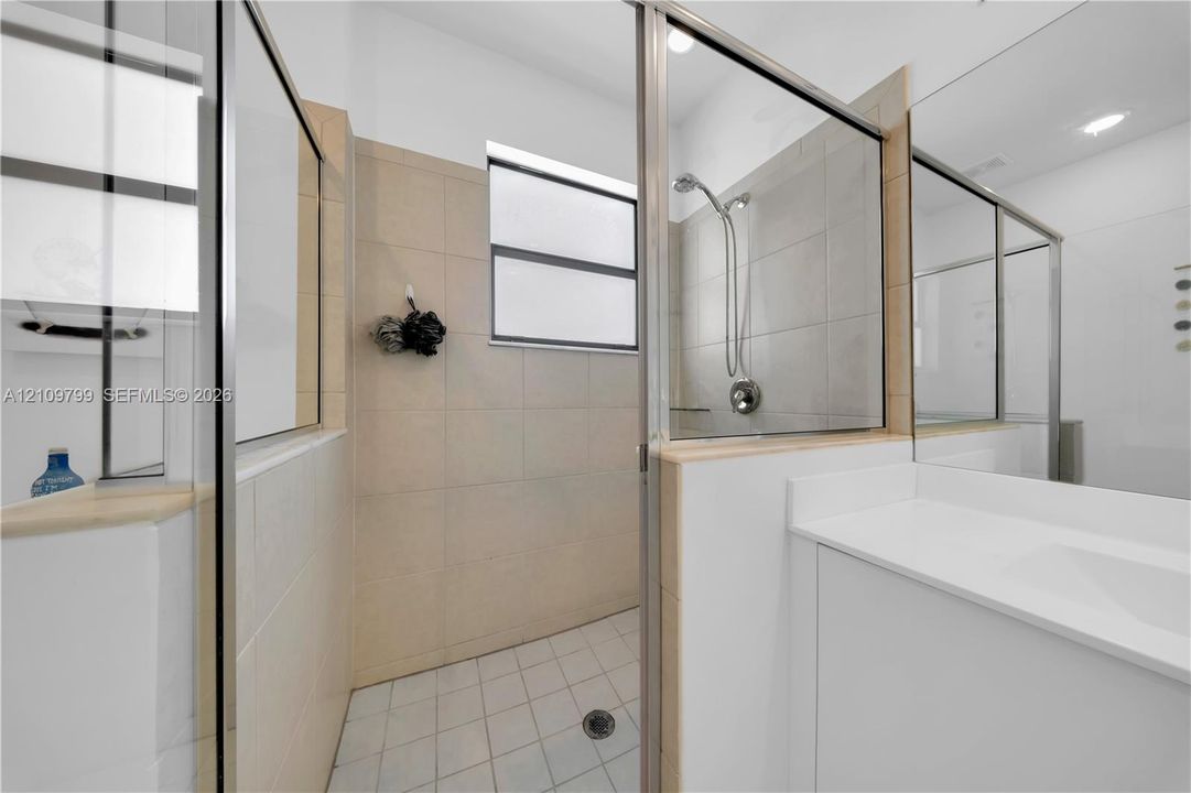 Walk-in shower featuring glass paneling, tile wall surround, and metal shower hardware, paired with a white vanity featuring a solid surface countertop