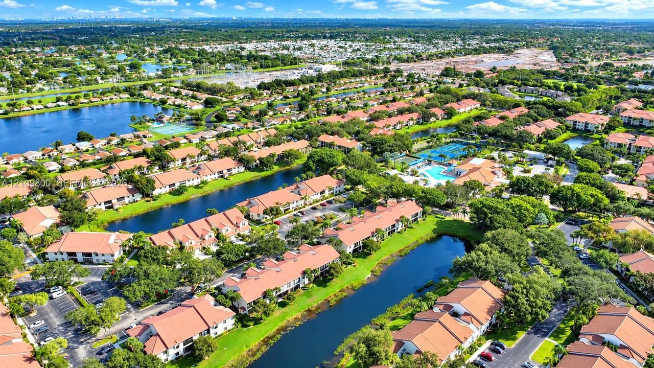Aerial perspective of a multi-unit residential complex featuring barrel tile roofing, surface parking, landscaped grounds, and bodies of water