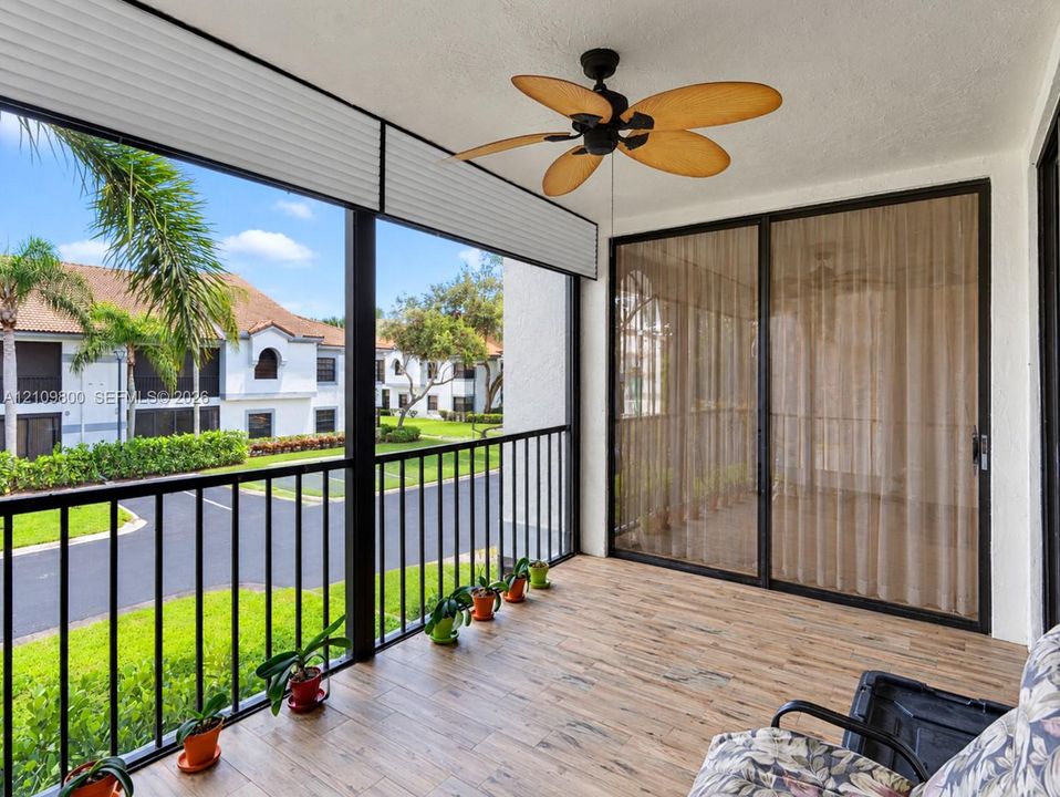 Screened-in balcony featuring wood-finish flooring, metal railing, retractable sun shades, and a ceiling fan