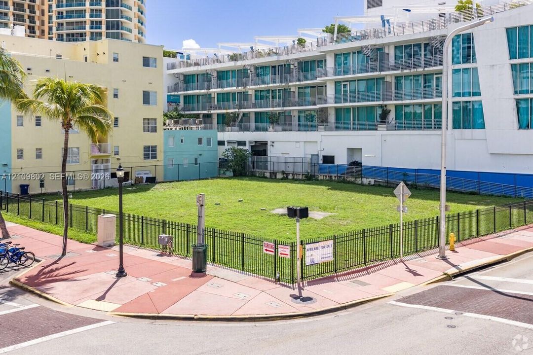 Cleared corner lot enclosed by black metal fencing, featuring level terrain and an established palm tree