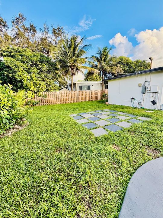 Backyard featuring a grass lawn, wood-panel fencing, paved stone accent area, and mature palm trees