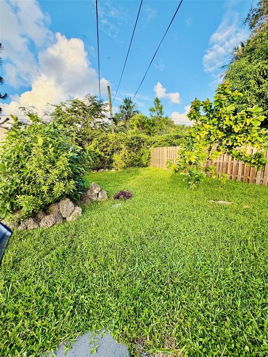 Expansive backyard featuring a manicured lawn, natural stone landscaping, perimeter wood fencing, and mature greenery