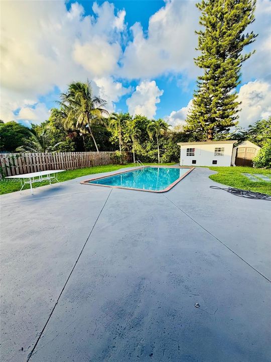In-ground swimming pool with concrete decking, fenced perimeter, and detached storage structure