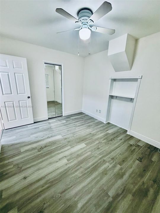 Room featuring wood-finish flooring, a ceiling fan with integrated lighting, a recessed wall niche with built-in shelving, and a closet with mirrored sliding doors