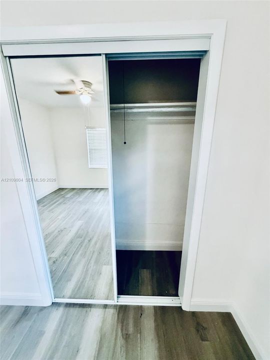 Closet featuring dual sliding mirrored doors and a built-in metal hanging rod, complemented by wood-finish flooring