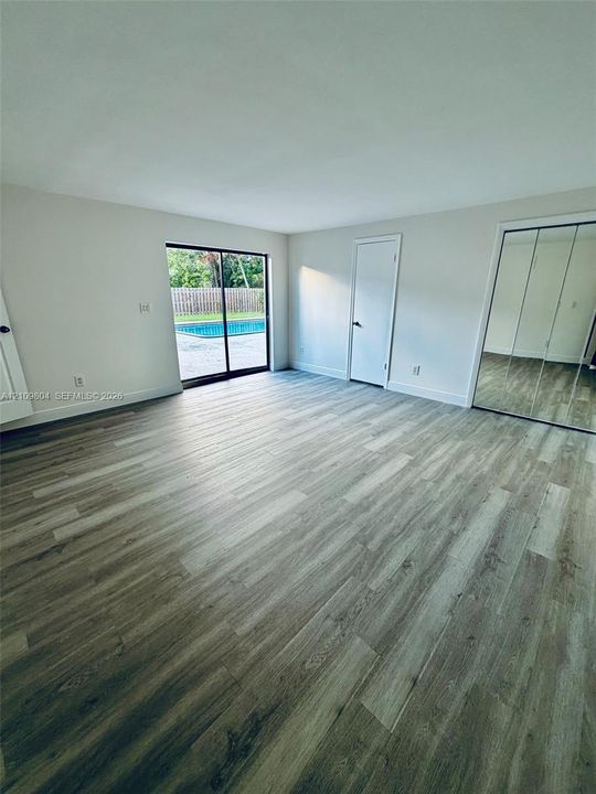 Neutral-toned interior featuring wood-finish flooring, mirrored closet doors, and a sliding glass door with exterior pool access