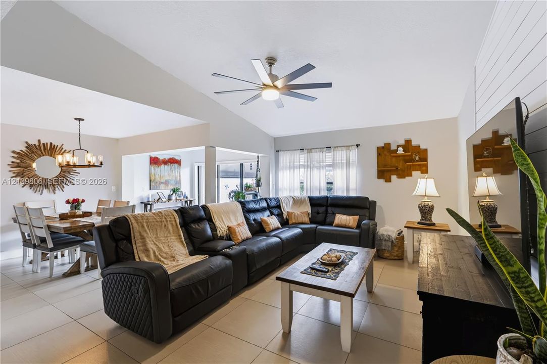 Vaulted ceilings featuring a multi-blade ceiling fan, neutral tile flooring, and white shiplap accent wall