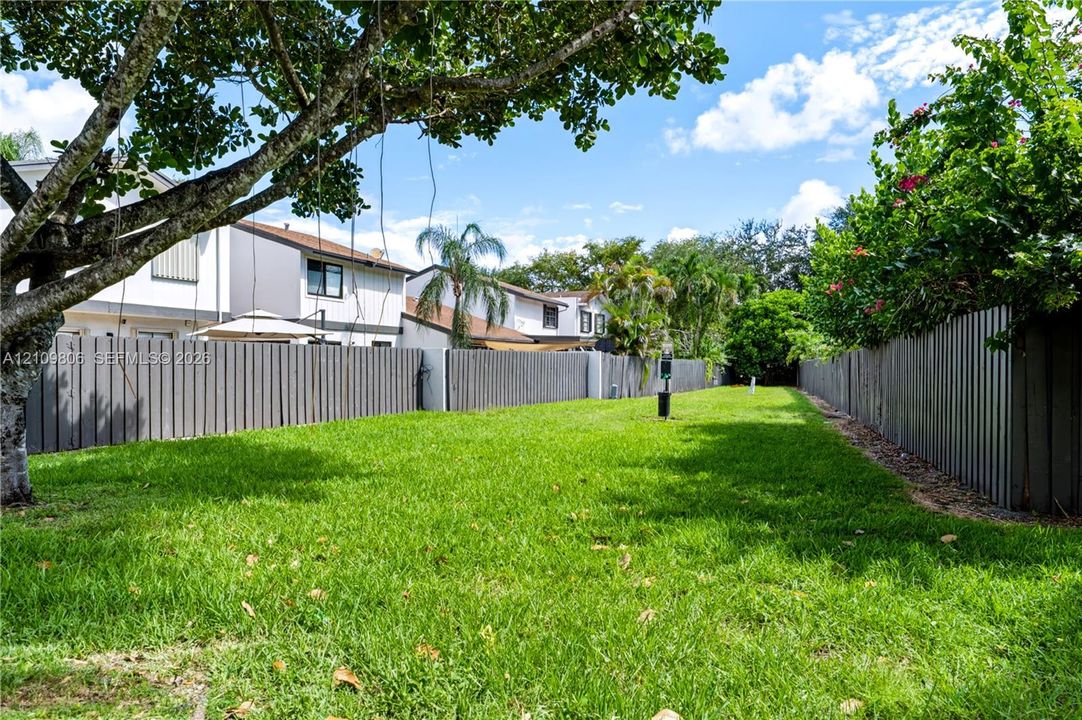 Private backyard featuring an expansive grassy lawn, perimeter wood fencing, and mature trees