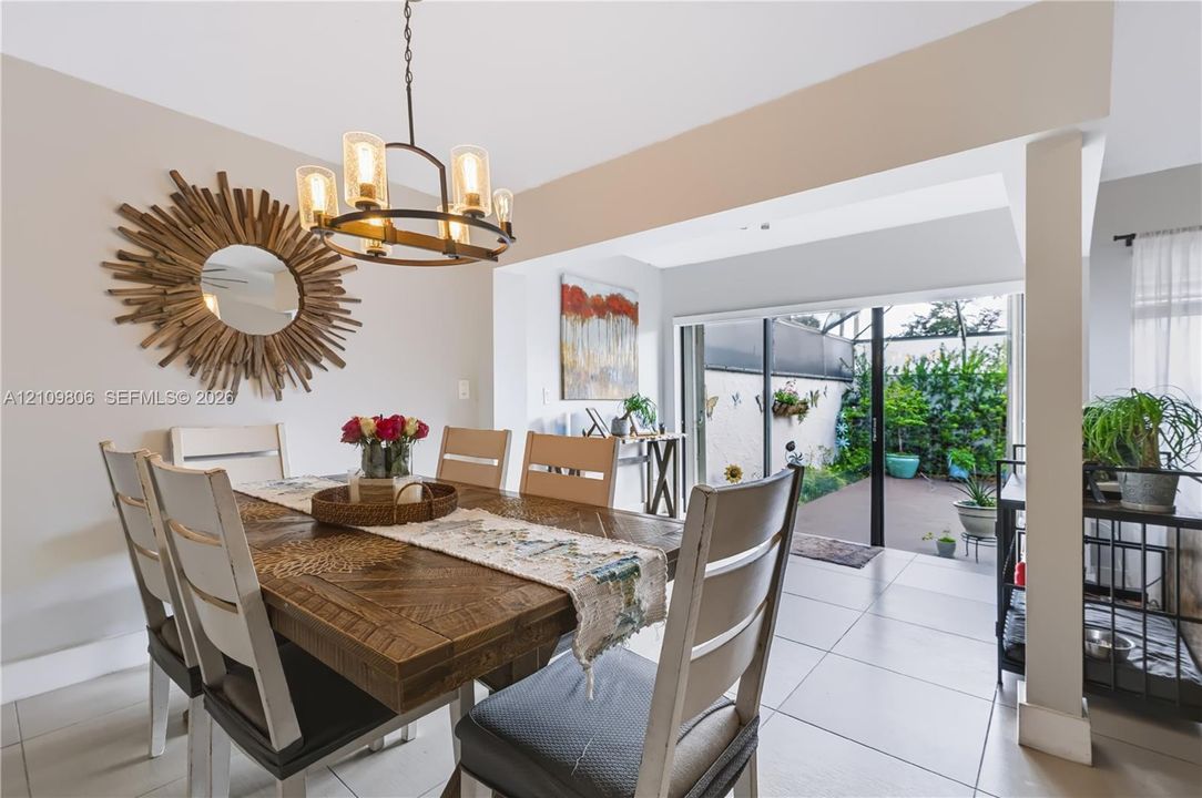 Dining area featuring large-format tile flooring, a circular multi-light chandelier, and sliding glass doors providing outdoor access to a private paved courtyard