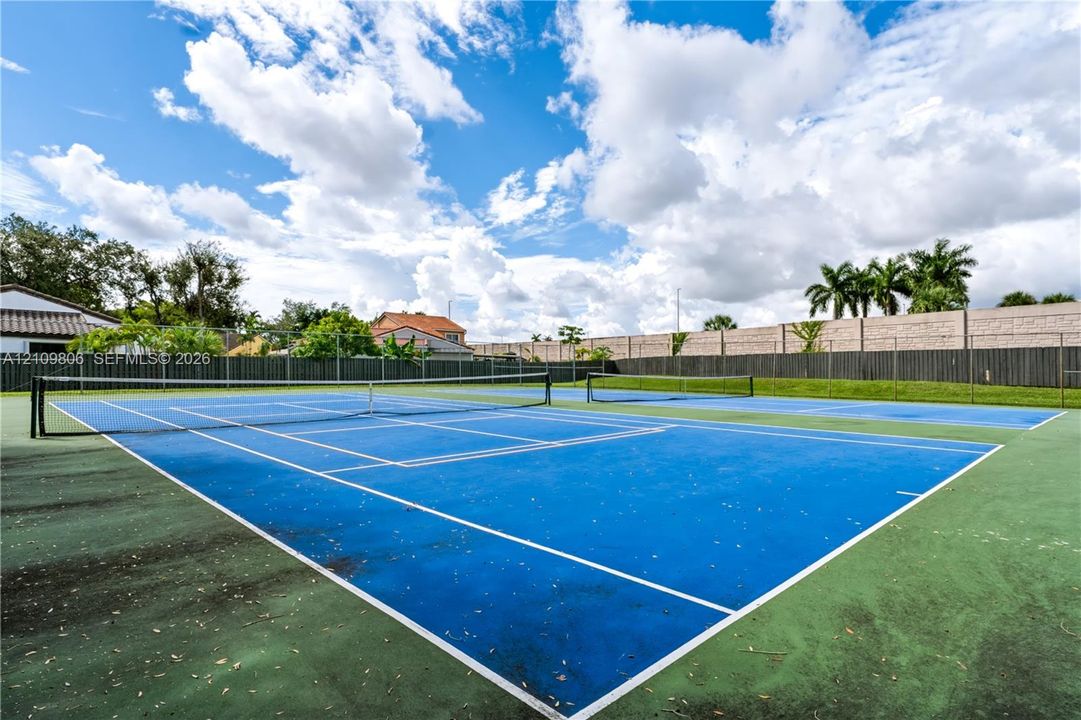Dual blue-surface tennis courts featuring perimeter chain-link fencing and concrete masonry boundary walls
