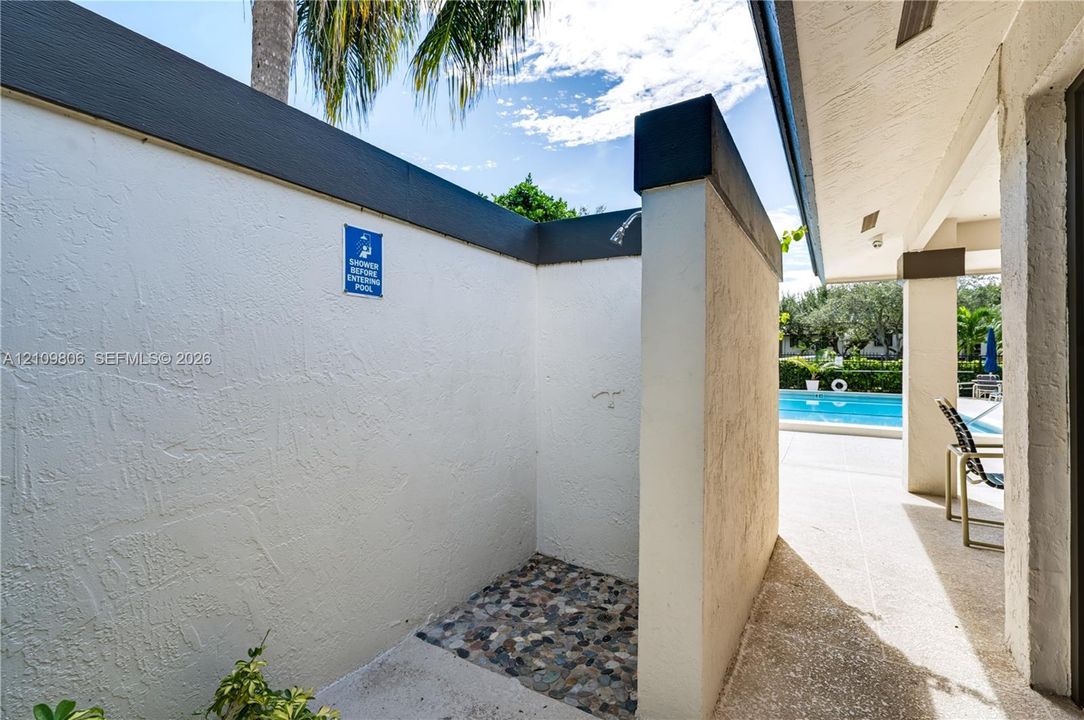 Outdoor shower area featuring textured privacy walls, a pebble-stone floor, and a wall-mounted showerhead