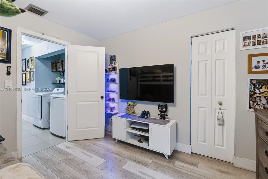 Interior room featuring wood-finish flooring, a bi-fold closet, and a standard interior door opening to a laundry area with tile flooring and built-in shelving