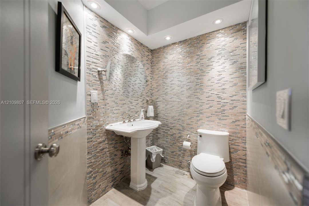 Powder room featuring a stacked-stone accent wall, pedestal sink, recessed lighting, and wood-finish tile flooring