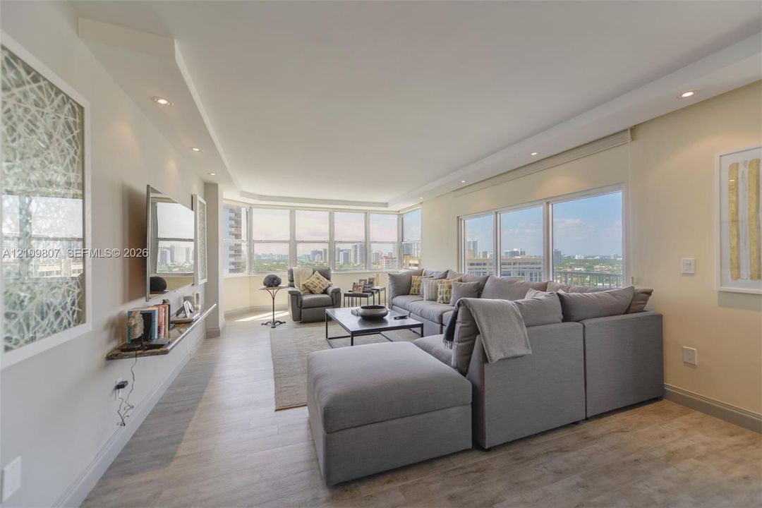 Living area featuring wood-finish flooring, extensive floor-to-ceiling windows, recessed ceiling lighting, and a wall-mounted stone shelf