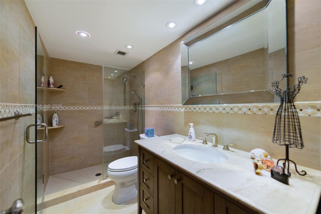 Bathroom featuring a vanity with stone countertop, beveled-edge wall mirror, recessed ceiling lighting, and a glass-enclosed shower with tiled walls