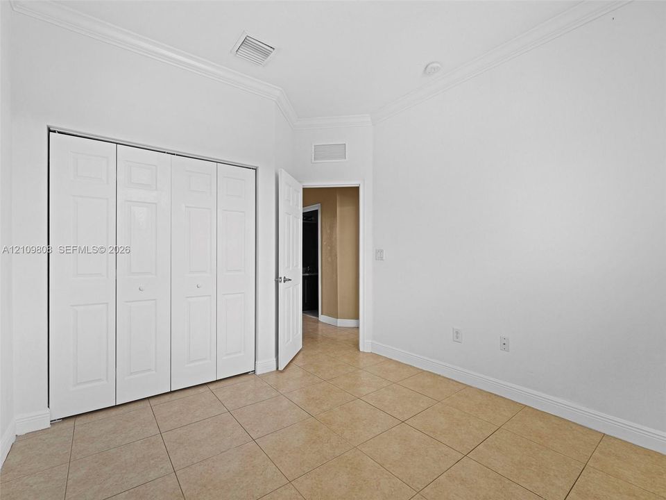 Neutral-toned tile flooring, white bi-fold closet doors, crown molding, and painted interior doors