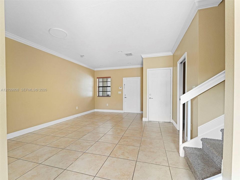 Interior space featuring neutral-tone tile flooring, crown molding, recessed lighting, and a white staircase railing