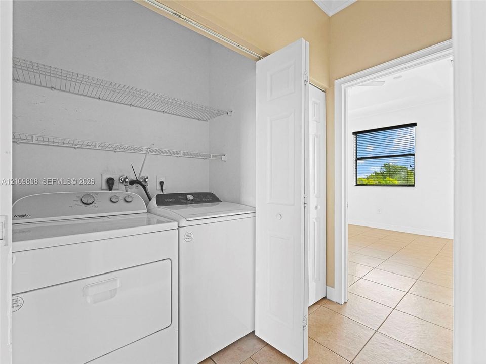 Laundry area featuring dual white bifold doors, integrated wire shelving, and tile flooring
