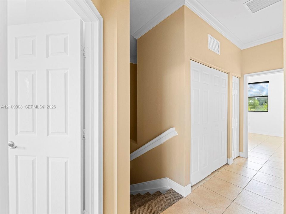 Interior hall featuring ceramic tile flooring, crown molding, double-panel closet doors, and white-trimmed door frames