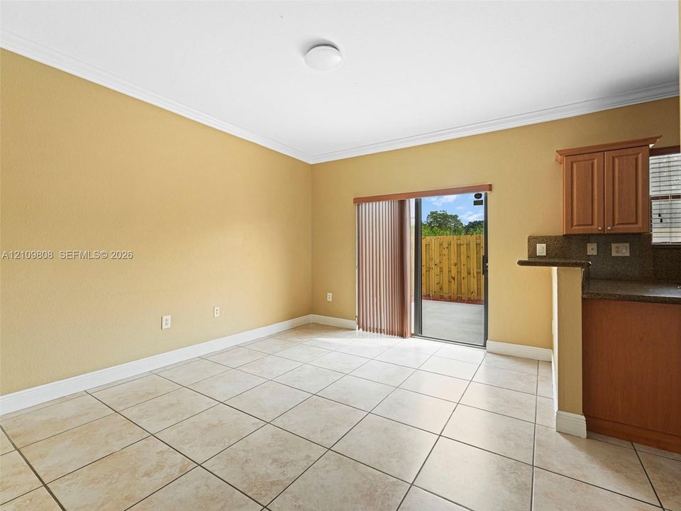 Neutral-toned interior featuring ceramic tile flooring, crown molding, a built-in kitchen peninsula with cabinetry, and a sliding glass door providing access to a concrete patio