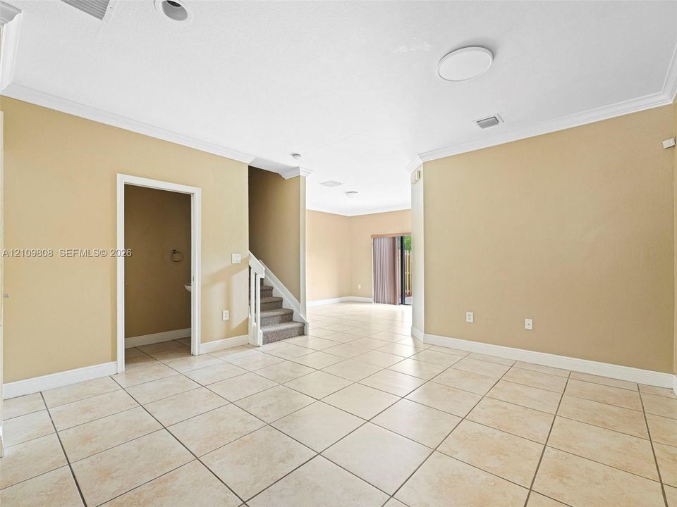 Open-concept interior featuring light-toned tile flooring, crown molding, recessed lighting, and a staircase with white balusters