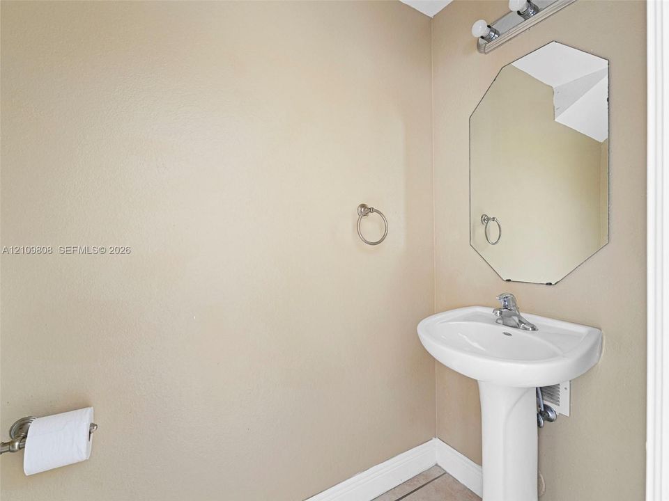 White porcelain pedestal sink, chrome faucet, octagonal wall-mounted mirror, and multi-light vanity fixture
