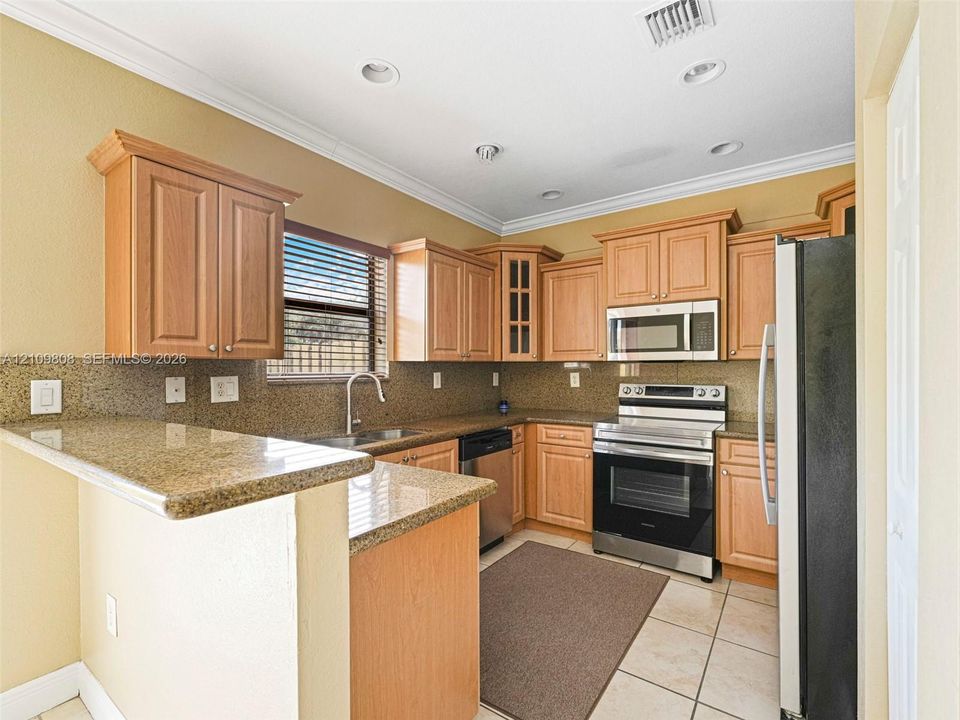 Kitchen featuring natural wood cabinetry, stone countertops, stainless steel appliances, a tile backsplash, and recessed lighting