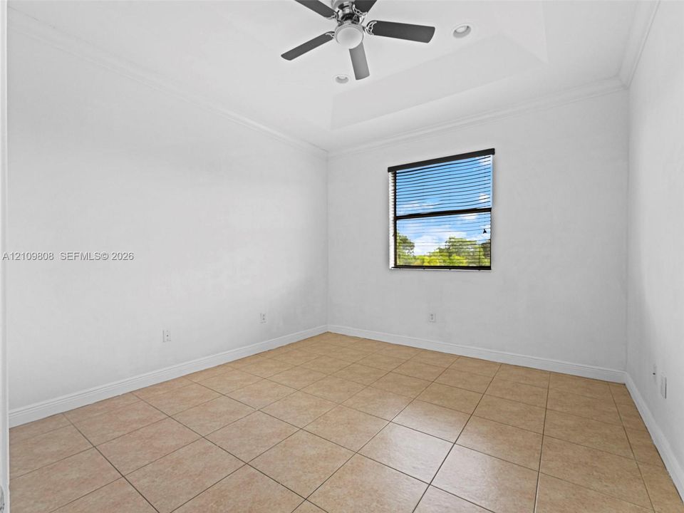 Room featuring a tray ceiling, ceiling fan, tile flooring, and a window with blinds