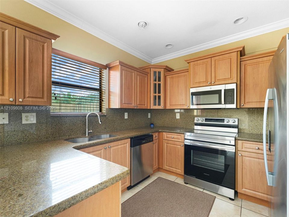 Kitchen featuring wood cabinetry, natural stone countertops, a stainless steel undermount sink with a gooseneck faucet, built-in stainless steel appliances, and recessed lighting