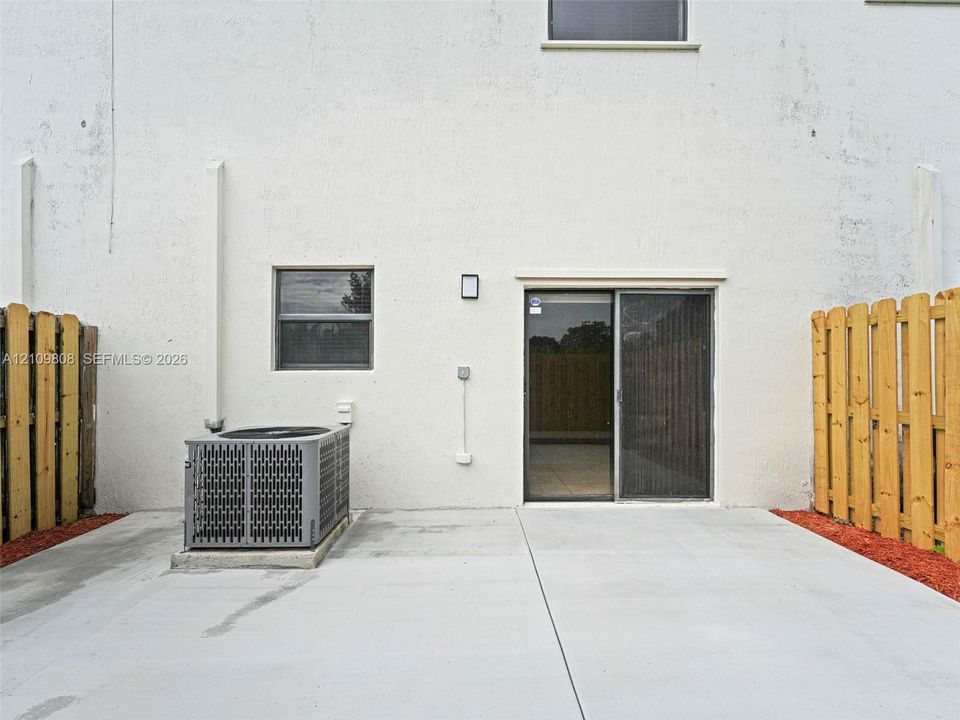 Concrete patio area featuring a sliding glass door, a window with a dark frame, and wood-slat privacy fencing