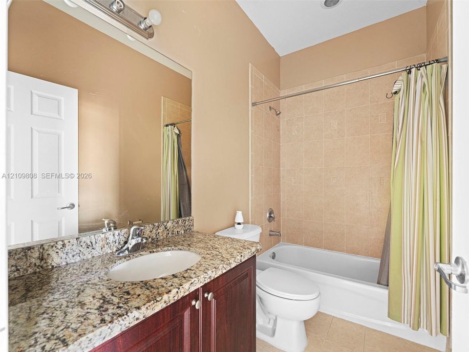 Bathroom featuring a vanity with stone-finish countertop, undermount sink, dark wood-tone cabinetry, and a full-height tile surround in the tub-shower combination