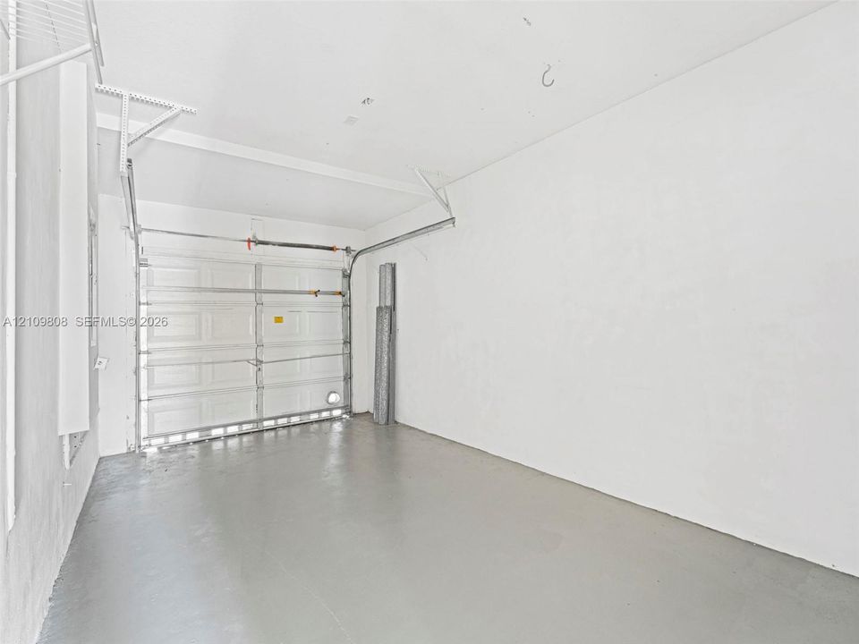 Garage interior featuring white finished walls, a sectional roll-up garage door, painted concrete flooring, and ceiling-mounted storage shelving